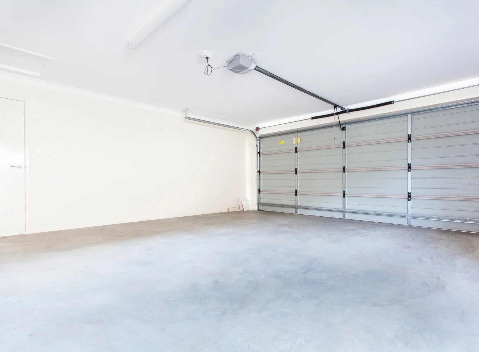 Empty garage with white walls, concrete floor, and a large grey roll-up door.