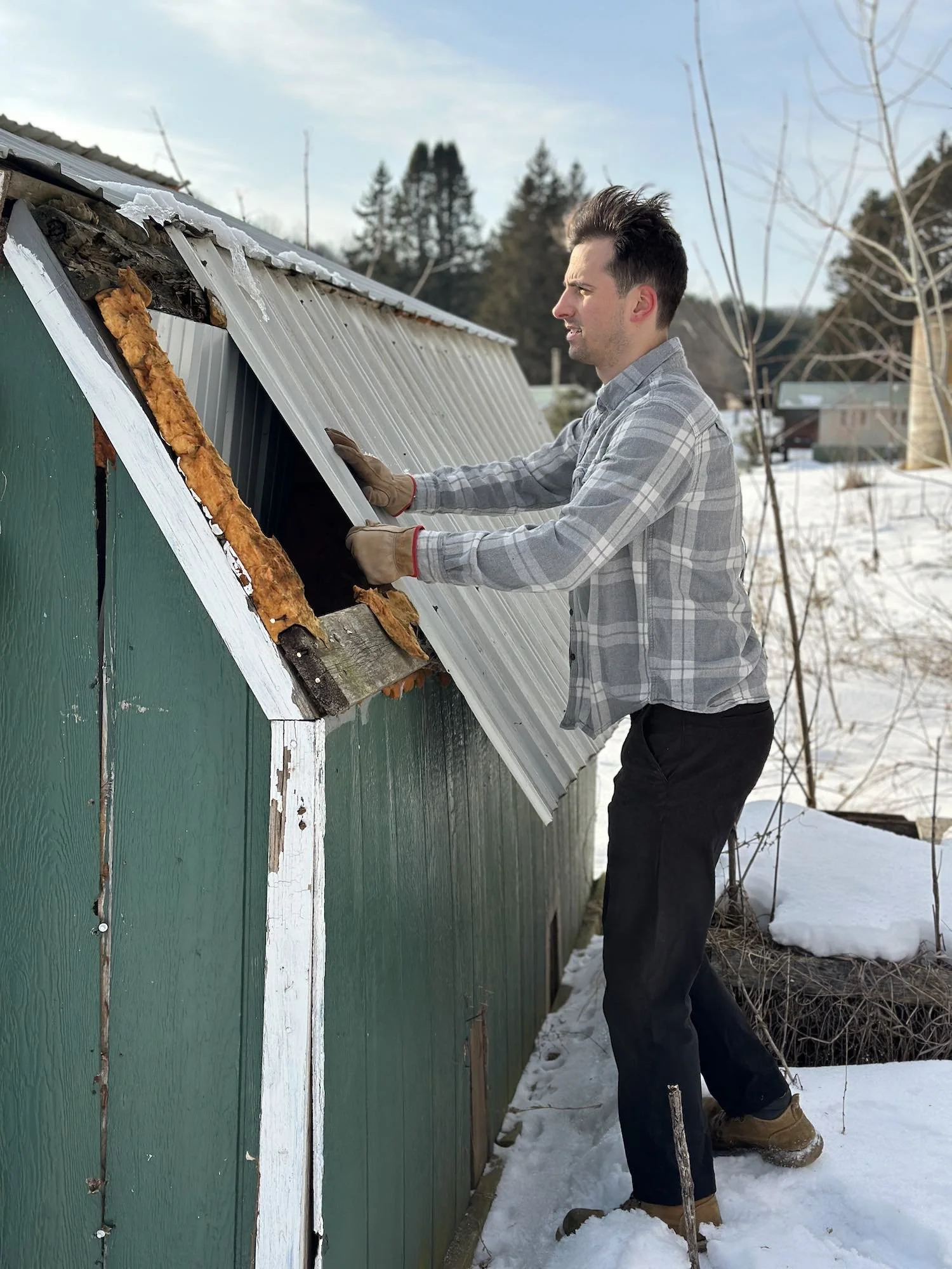 Man repairing a roof on a green shed with snow on the ground in winter.