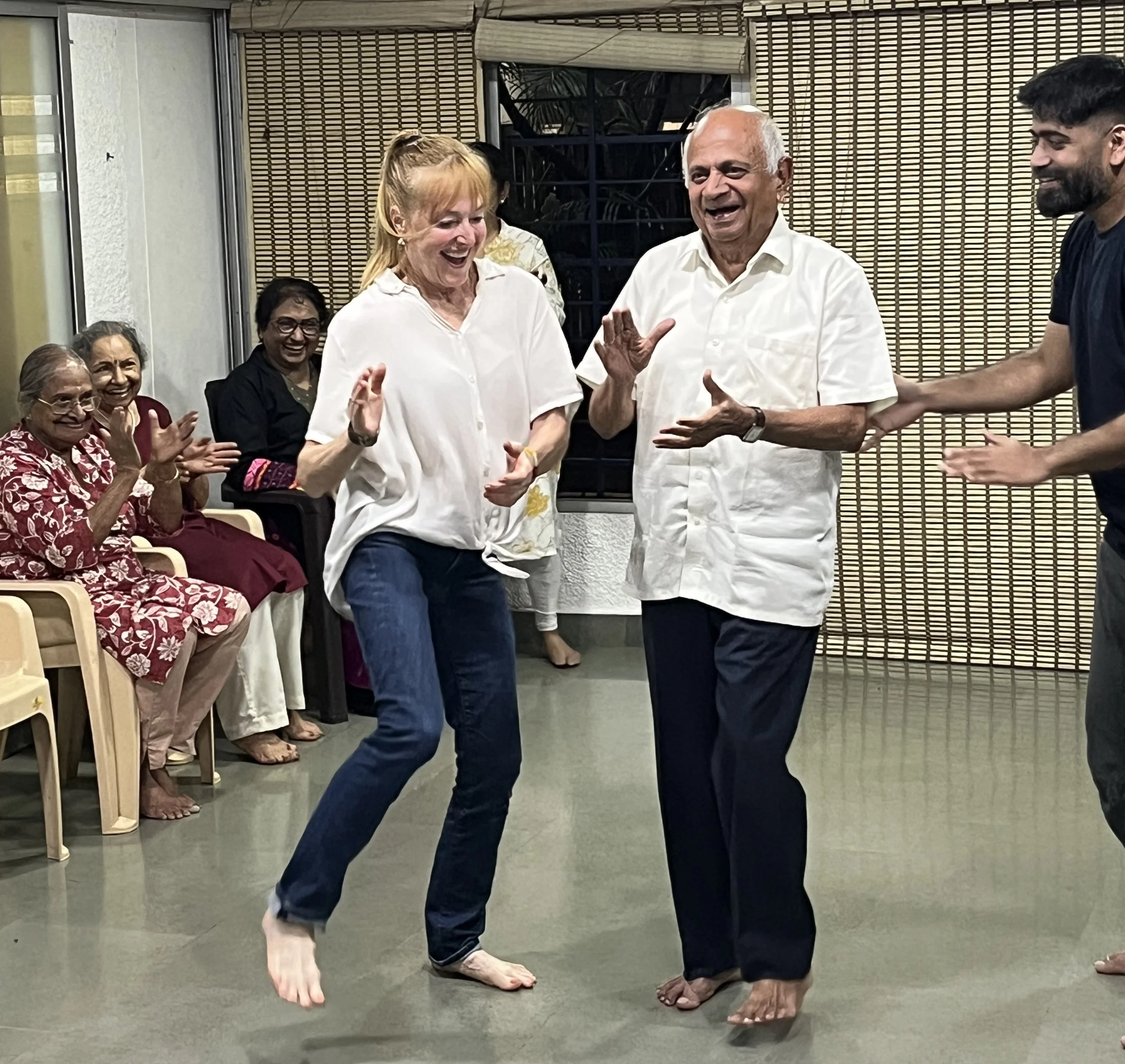 Red-haired Lucy Bowen dancing with a Parkinson's dancer in Pune India with his teacher, Hrishikesh Pawar, a middle-aged Indian man, standing nearby watching and smiling