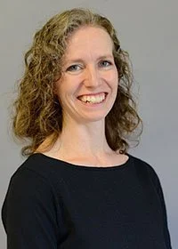 Woman with curly hair smiling, wearing a black top