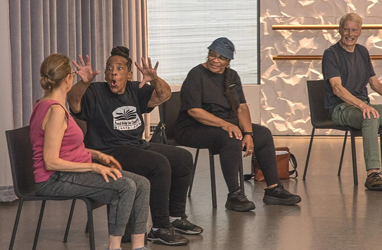 Dance for PD participants sitting on chairs. One dancer is gesturing animatedly.