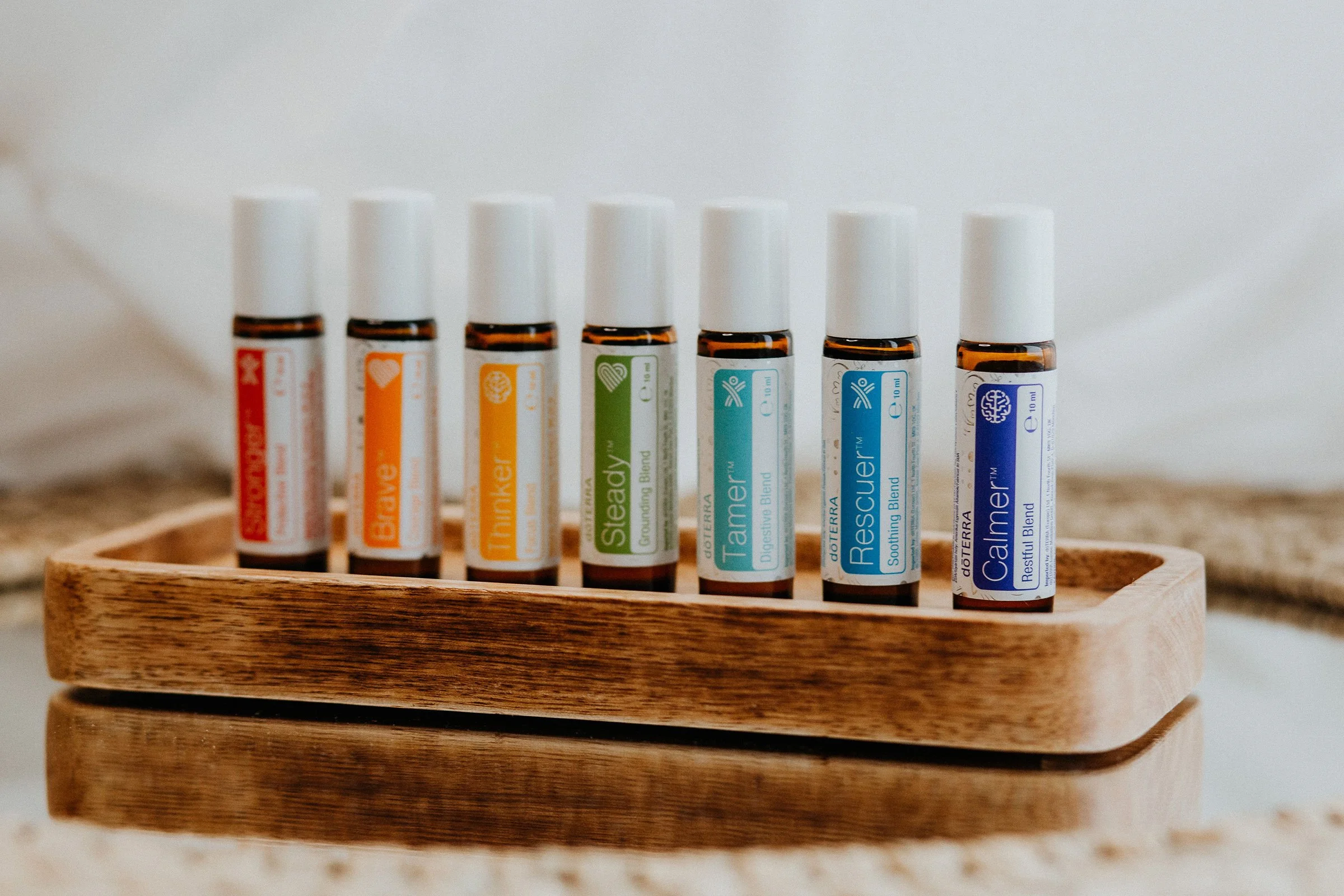 Sieben ätherische Öle in kleinen Fläschchen, das auf einem handgefertigten Holztablett stehen, mit weißem Hintergrund.