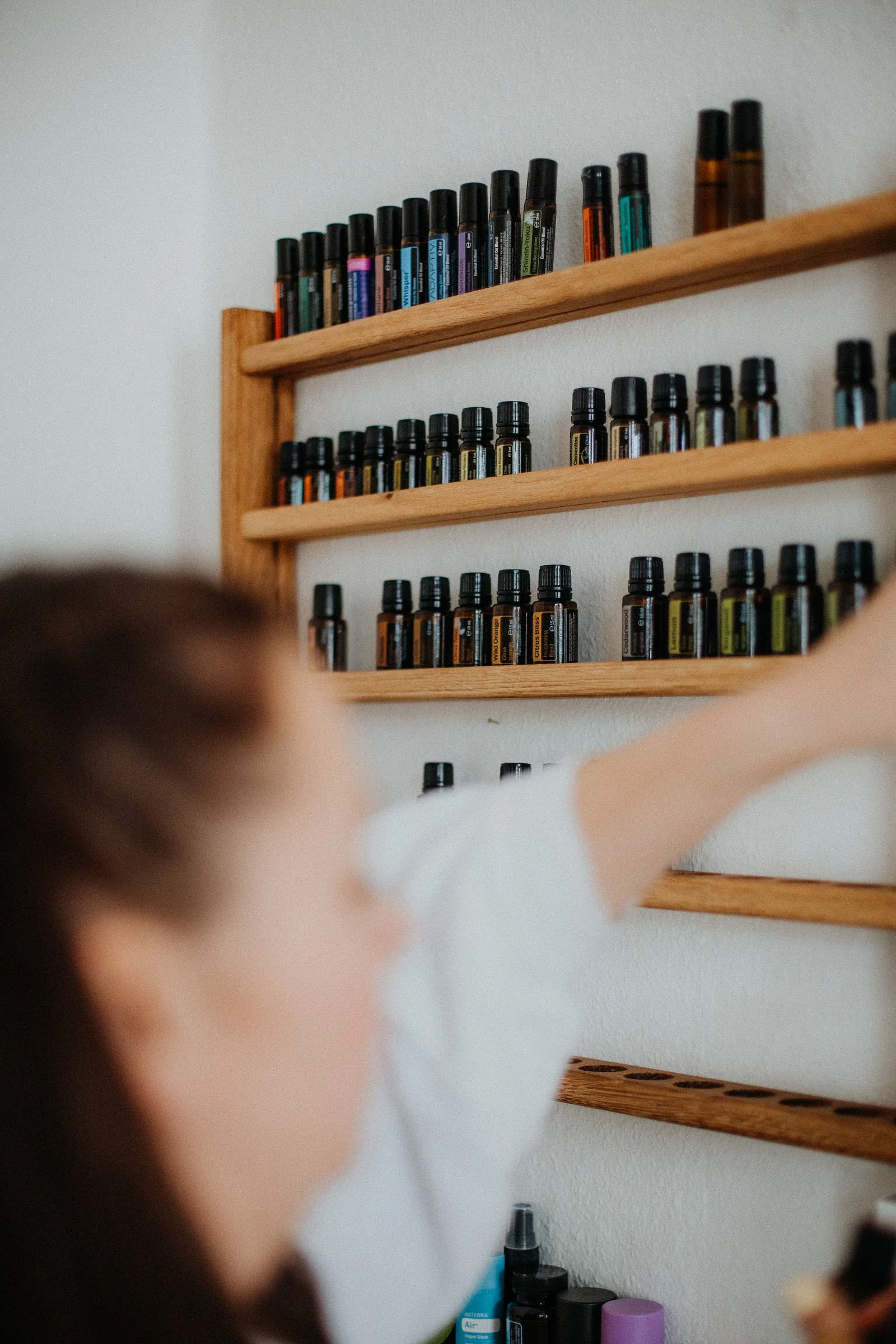 Ein Kind mit braunen Haaren, die nach links schauen, ist in einem Raum, der mehrere Holzregale an der Wand hat. Auf den Regalen befinden sich zahlreiche kleine Fläschchen und Ätherische Öle.