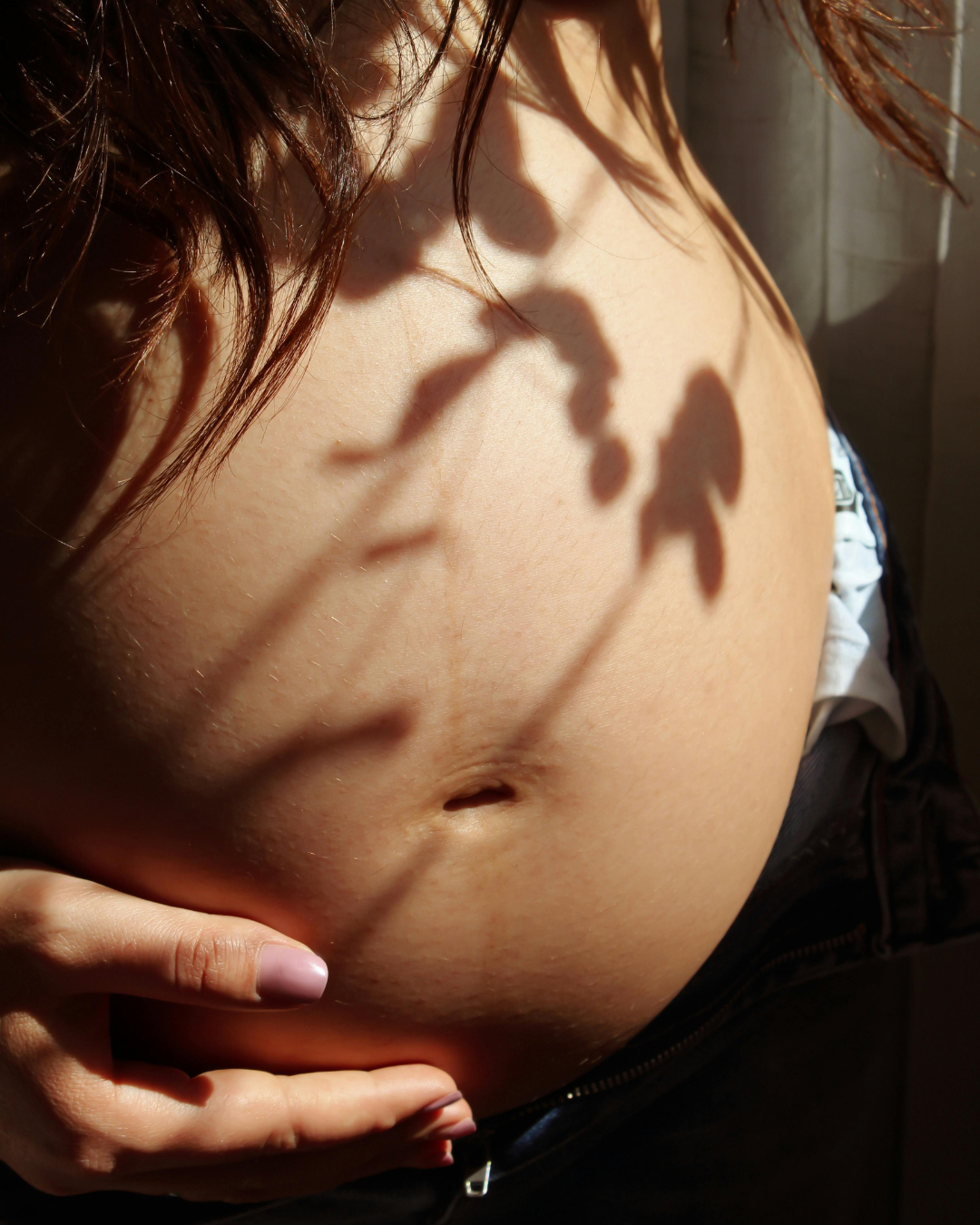 Nahaufnahme eines menschlichen Bauches mit Schatten eines Blattes darauf, eine Person streicht ihren Bauch.