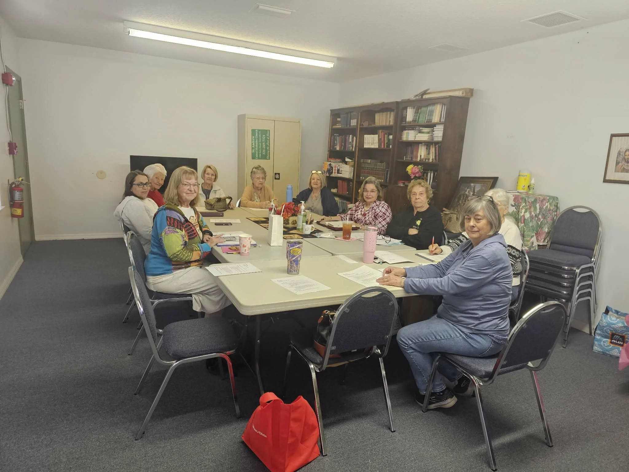 Group of women sitting around a conference table in a meeting room, with papers, drinks, and personal items on the table.