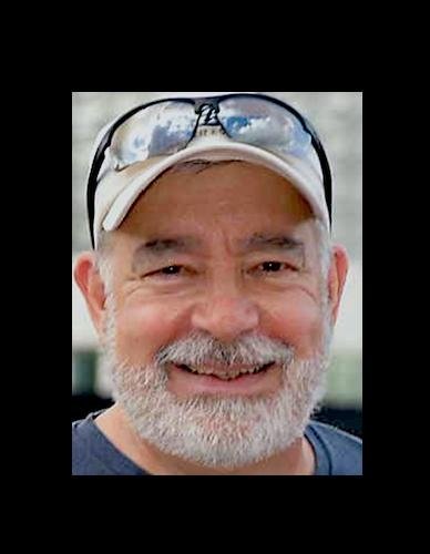 Close-up of a smiling older man with a beard and mustache, wearing a white cap and sunglasses on his forehead.