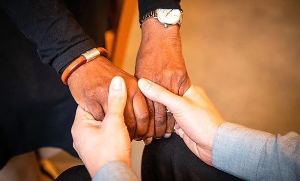 Three people holding hands in a circle, symbolizing unity and support.
