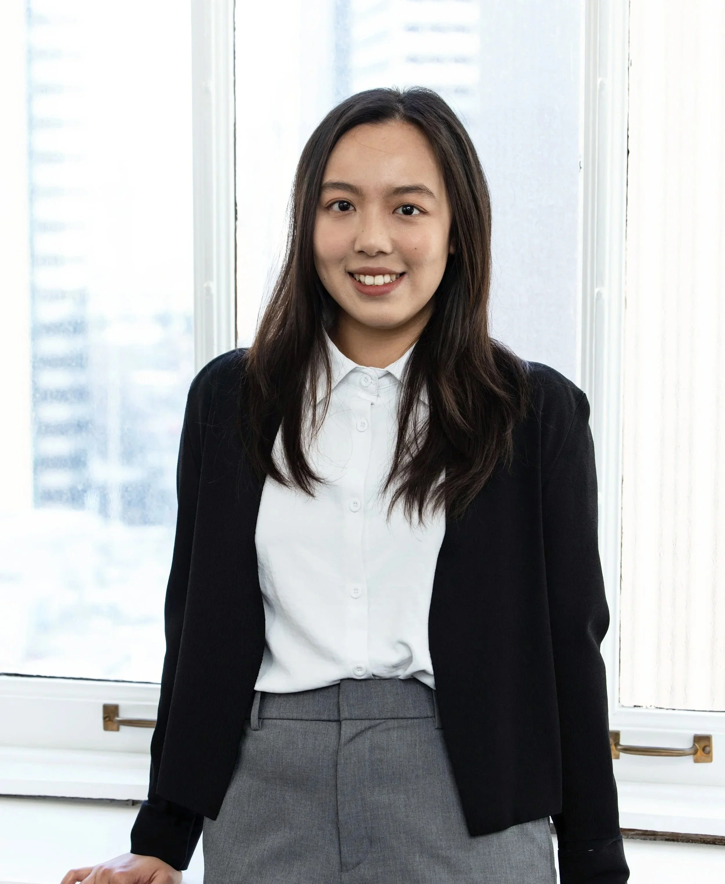 Cherrie Li, a woman in business attire standing in front of a window with a cityscape view. She's a member of the BASE Design Structural Engineering firm in San Francisco.