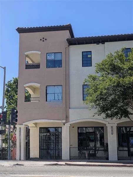 Three-story building with a beige and white facade, balconies on the second and third floors, and a tree partially in front. Structural engineering by BASE Design in San Francisco.