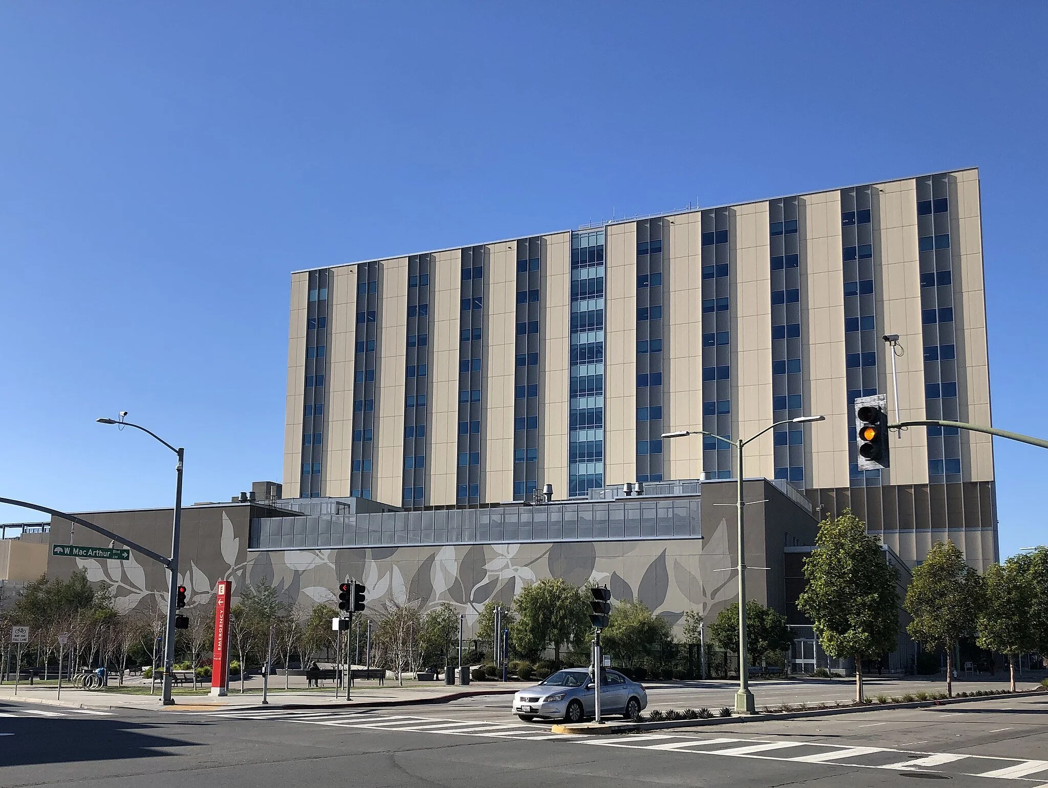 Kaiser Hospital Oakland, a large beige building with blue glass windows, located at a street corner with traffic lights.  Ongoing structural engineering support by BASE Design in San Francisco.