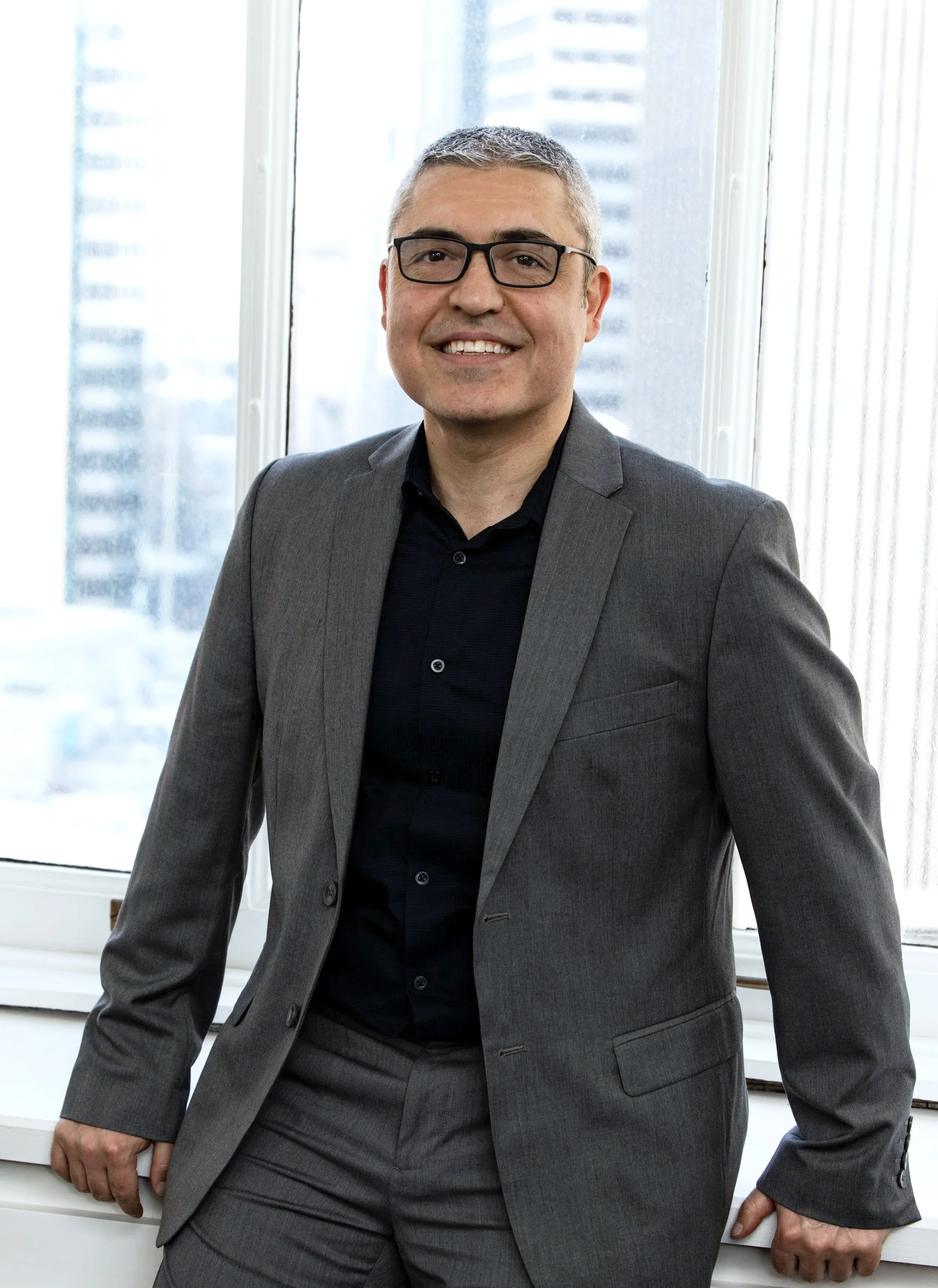Gokhan Akalan, Principal of BASE Structural Engineering in San Francisco, poses in front of his office window in a professional portrait.