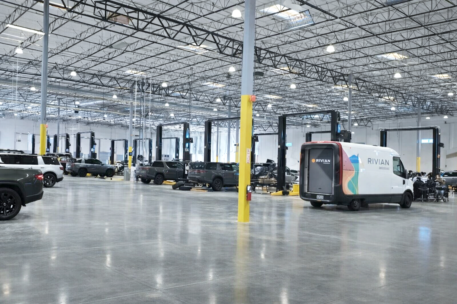 Large indoor parking garage with multiple cars and a Rivian delivery van, with high ceilings and industrial lighting. Structural engineering by BASE Design in San Francisco.
