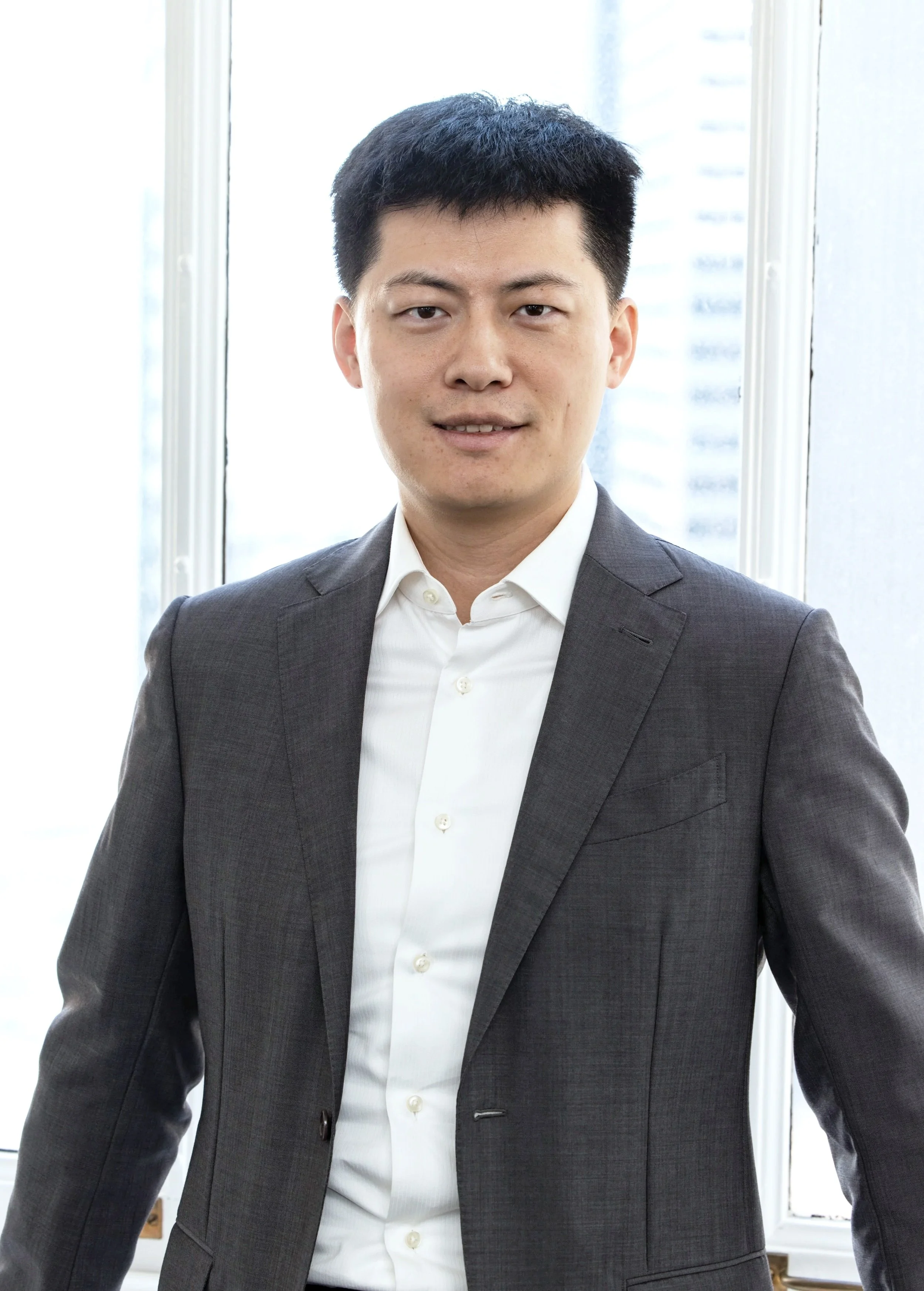 Jihong Li, senior project engineer for BASE Structural Engineering in San Francisco, poses in front of his office window in a professional portrait.