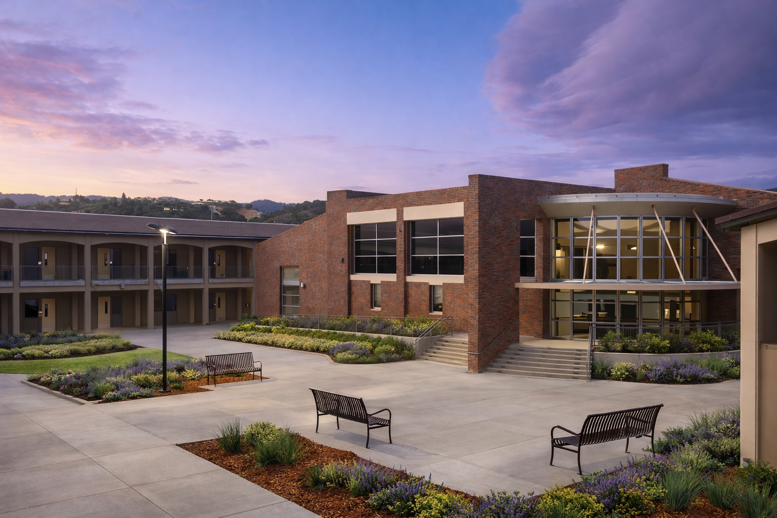 Modern school building with brick exterior and large glass windows, surrounded by landscaped gardens, benches, and pathway at dusk. Structural engineering by BASE Design in San Francisco.
