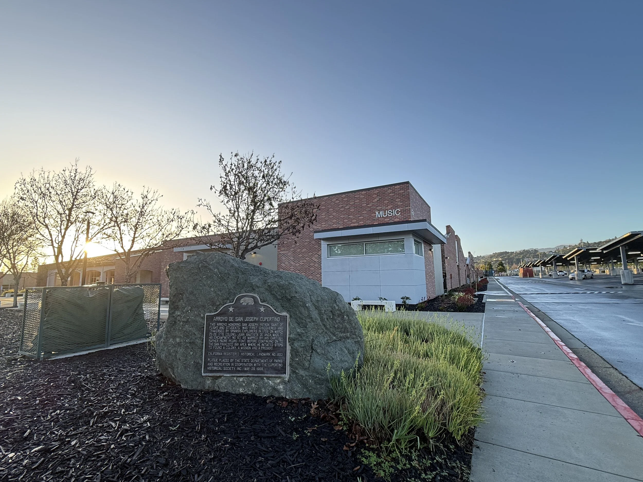 A brick building labeled 'Music' with a parking lot on the right and a historical marker on a large rock in the foreground, with leafless trees and a clear sky in the background. Structural engineering by BASE Design in San Francisco.