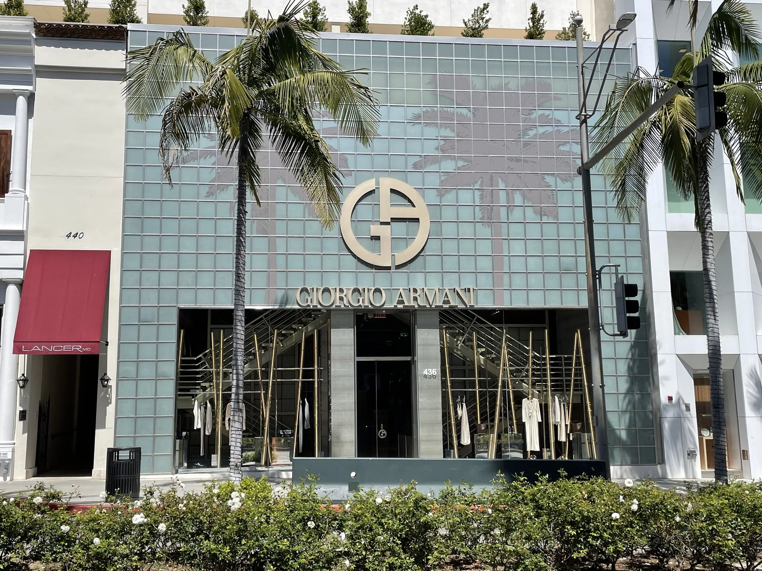 The Giorgio Armani store in Beverly Hills, CA, featuring a modern glass facade, gold accents, and palm trees in front. The store's logo and name are prominent above the entrance. Structural engineering by BASE Design in San Francisco.