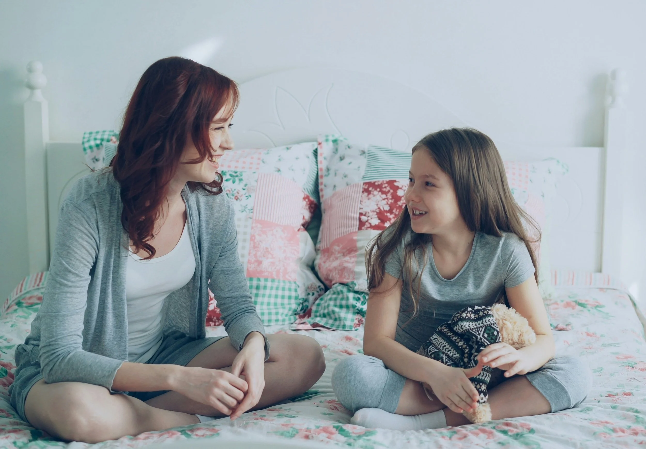 woman and girl sit on bed smiling