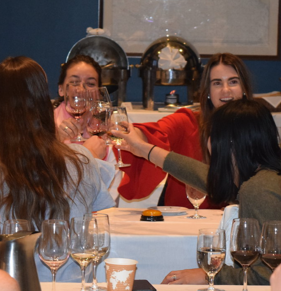 A group of women raising wine glasses in a toast at a dinner party.