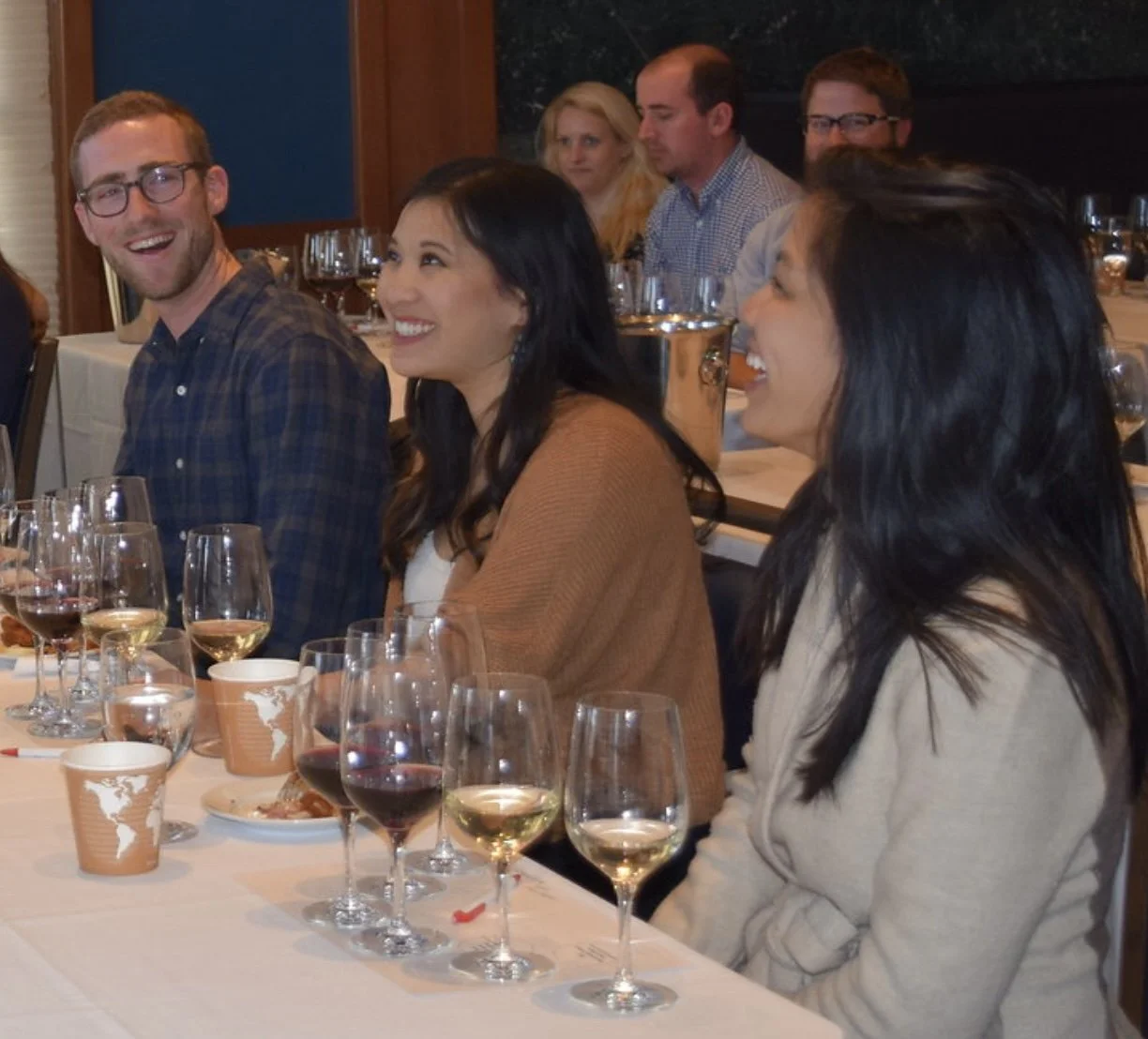 People sitting at a wine tasting with wine glasses, enjoying an educational session.
