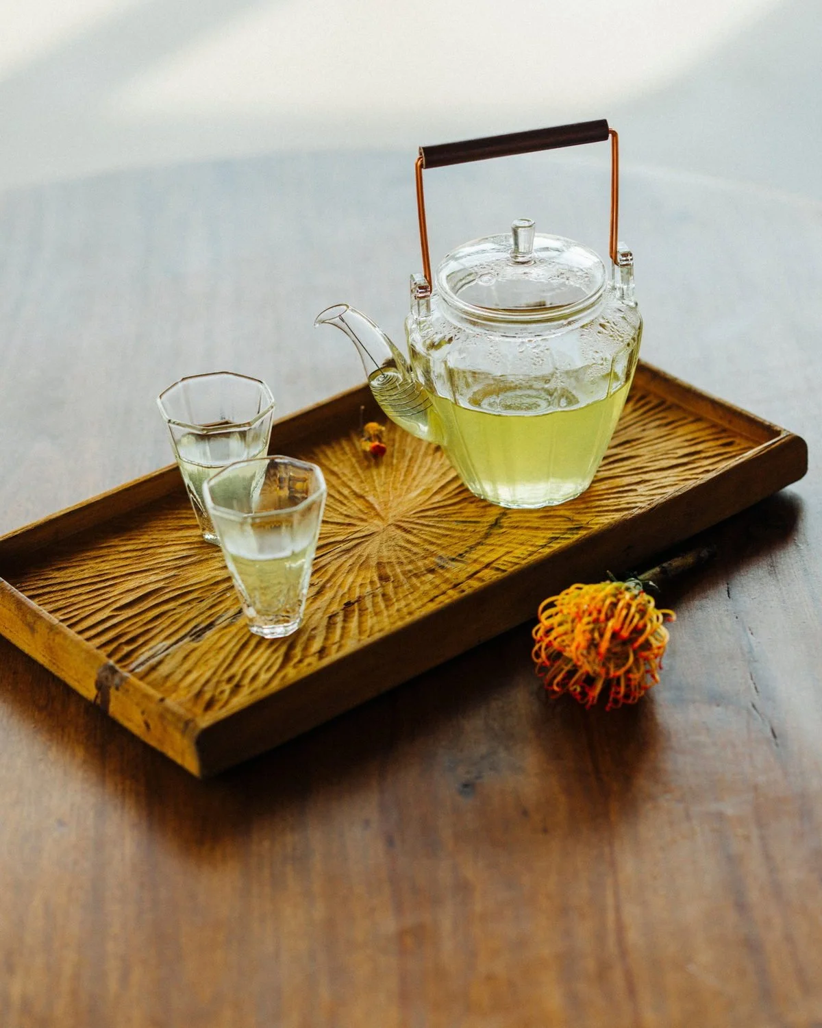 Chrysanthemum tea in a glass teapot and two small glasses on a carved wooden tray.