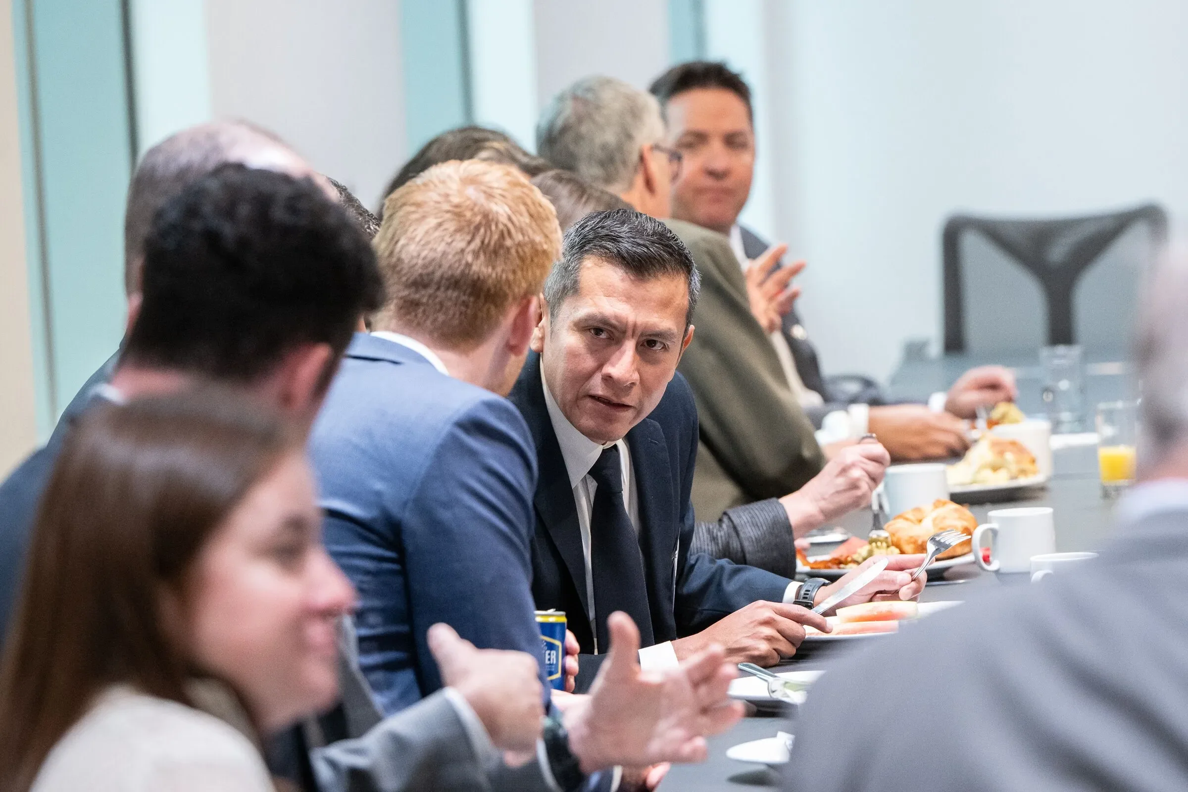 Business meeting with people sitting around a table, engaged in conversation, with breakfast items like croissants, coffee, and juice.