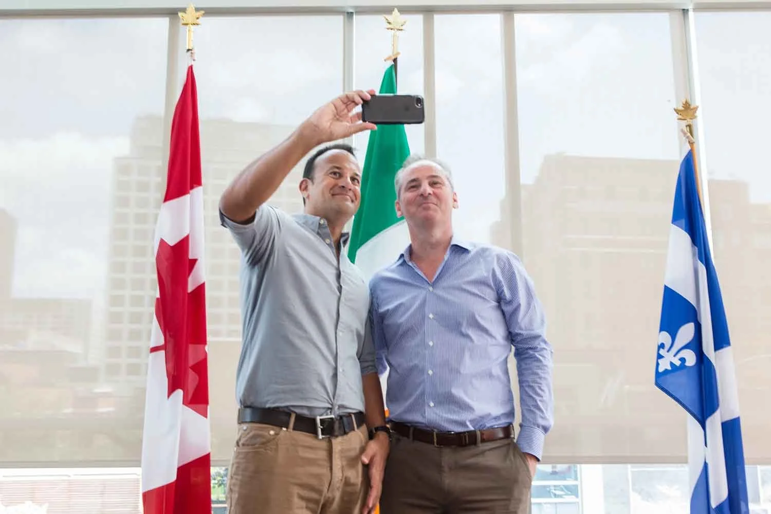 Two men taking a selfie in front of Canadian, Mexican, and Quebec flags.