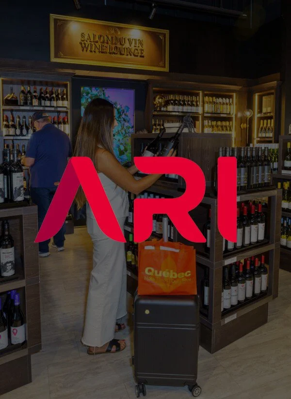 A woman shopping for wine at a liquor store, with shelves filled with wine bottles in the background and a large ARI logo overlayed in red.