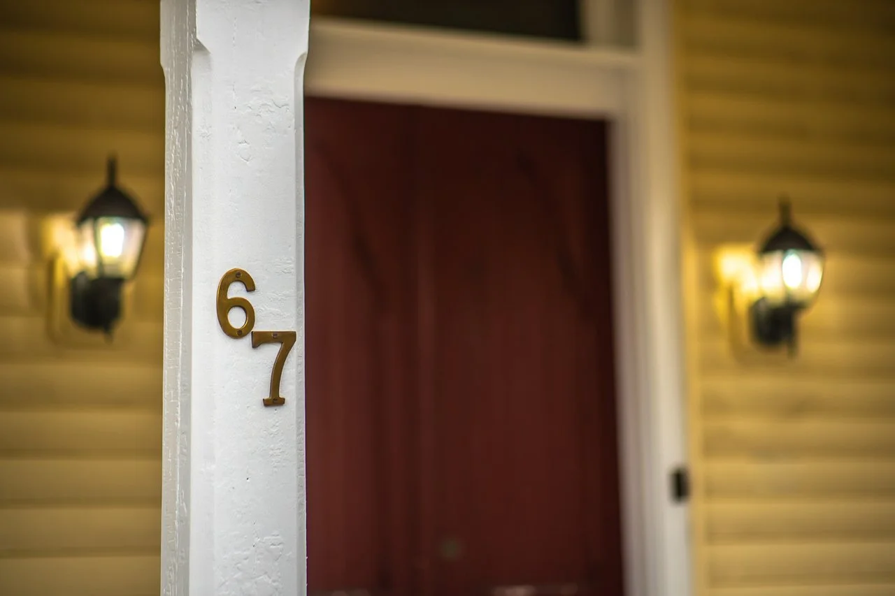 67 Byberry Rd, House number 67 on a white pillar with a red door and yellow interior walls, with exterior wall-mounted black lanterns on each side.