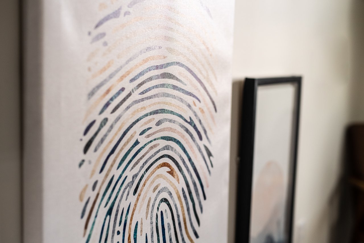 Close-up of a canvas with a fingerprint pattern in various colors, leaning against a wall, with a black frame next to it.