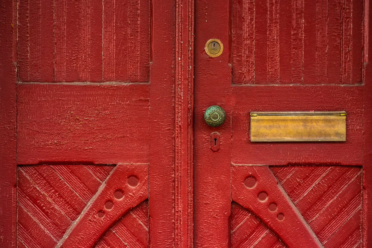 67 Byberry Rd, Red wooden double doors with visible grain, a brass doorknob, keyhole, and brass mail slot.