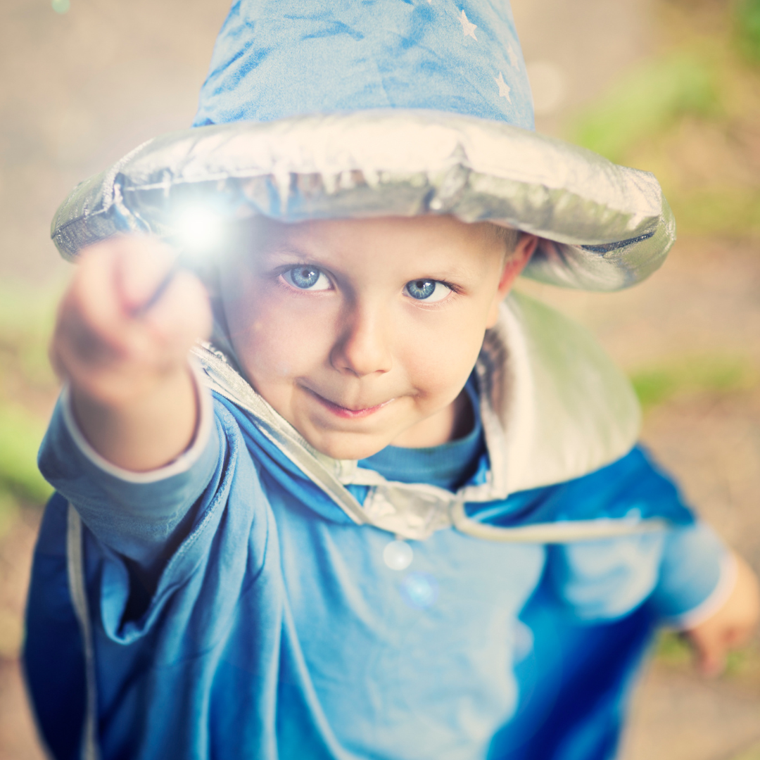 Small boy wearing blue wizard robes and pointing a magic wand directly at the viewer.