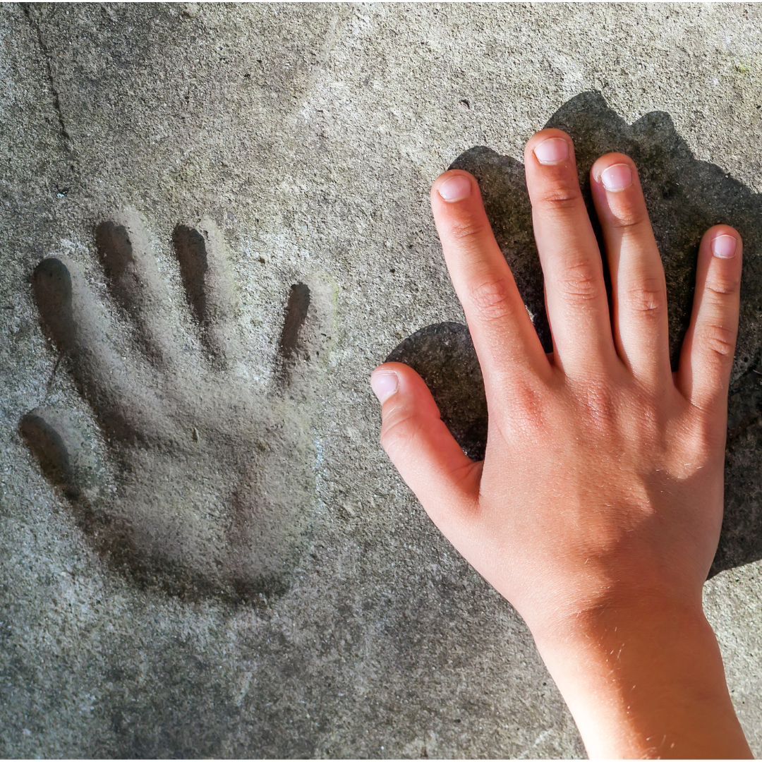 Picture of a handprint in stone next to a caucasian human hand