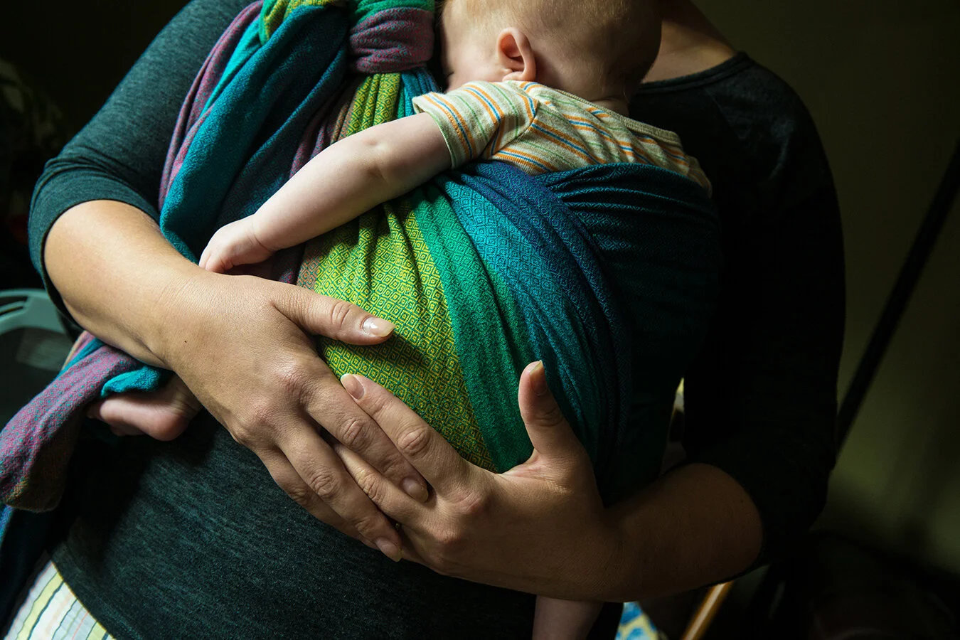 A person holding a sleeping child in a stretchy cloth wrap, close to the person's chest.