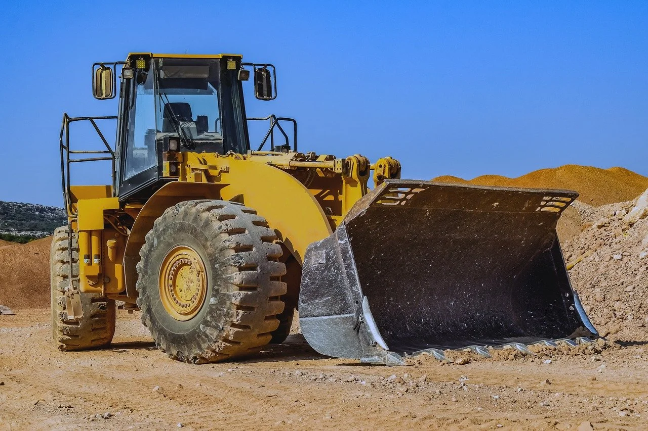 Un bulldozer jaune sur un chantier de construction avec des tas de terre derrière, sous un ciel bleu clair.