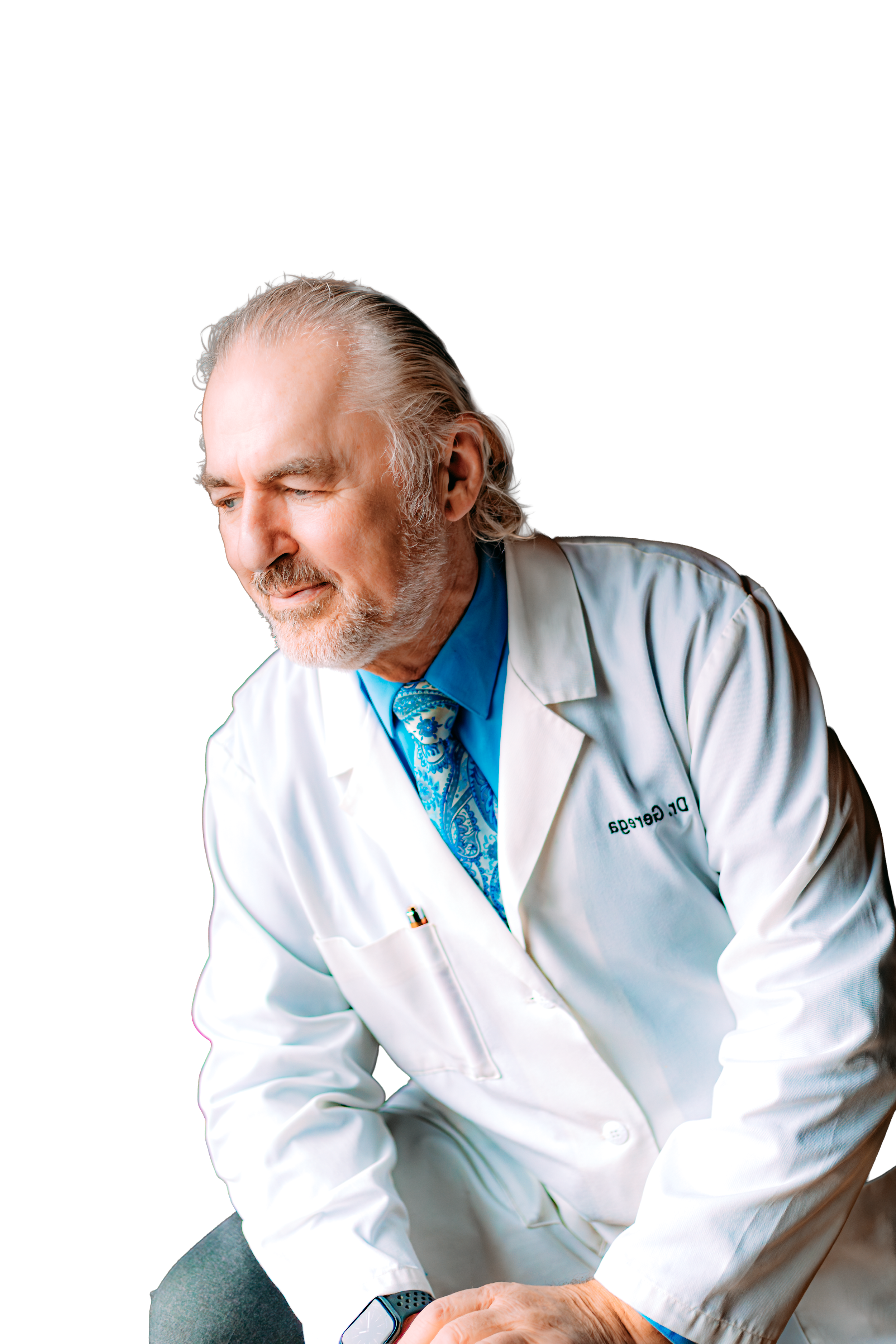 Elderly male doctor with white hair and beard, wearing a white lab coat, blue shirt, and patterned blue tie, looking contemplative with hands clasped, against a plain white background.