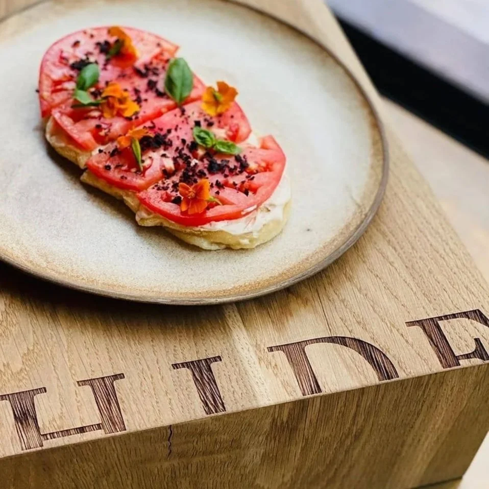 A plate with slices of tomato, basil leaves, and edible flowers on top, served on a wooden surface.