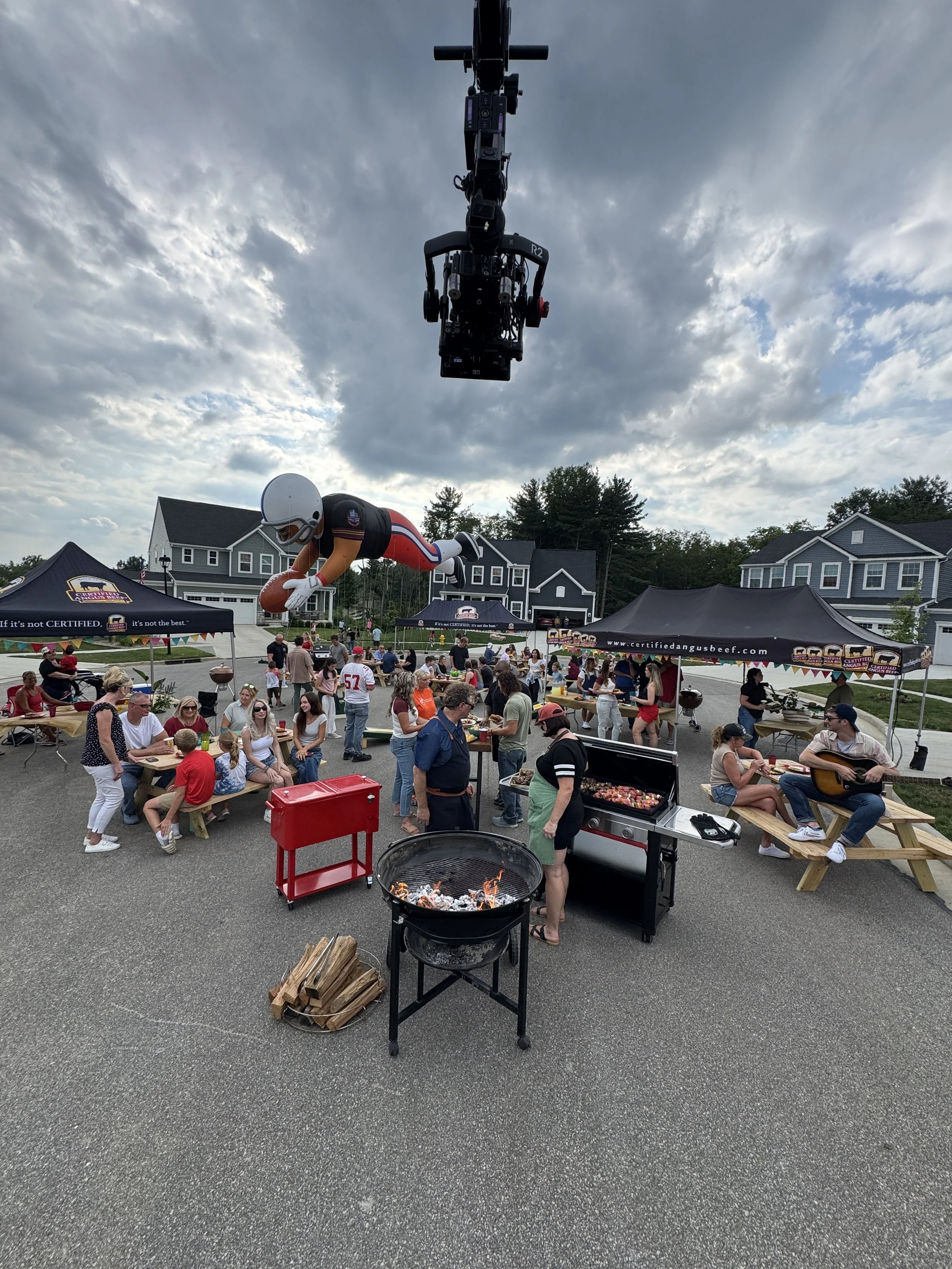 Camera crane filming a large outdoor commercial production with performers, crew, and branded event sets