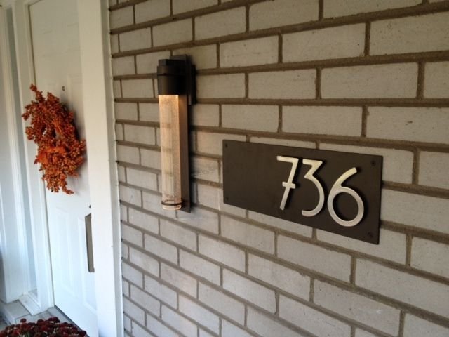 House address sign with the number 736 mounted on a brick wall near a front door with an autumn wreath.