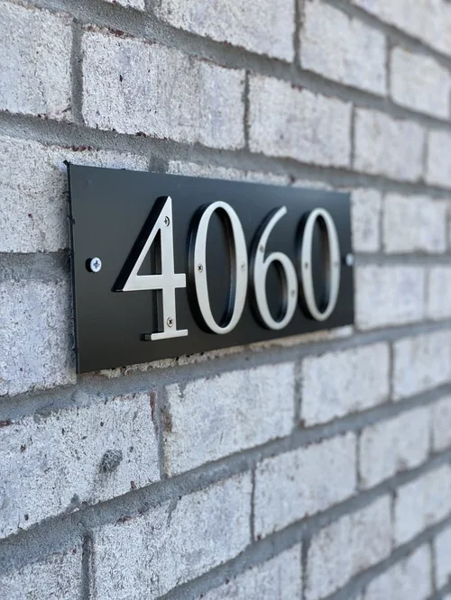 Building address plaque with the number 4060 mounted on a gray brick wall.