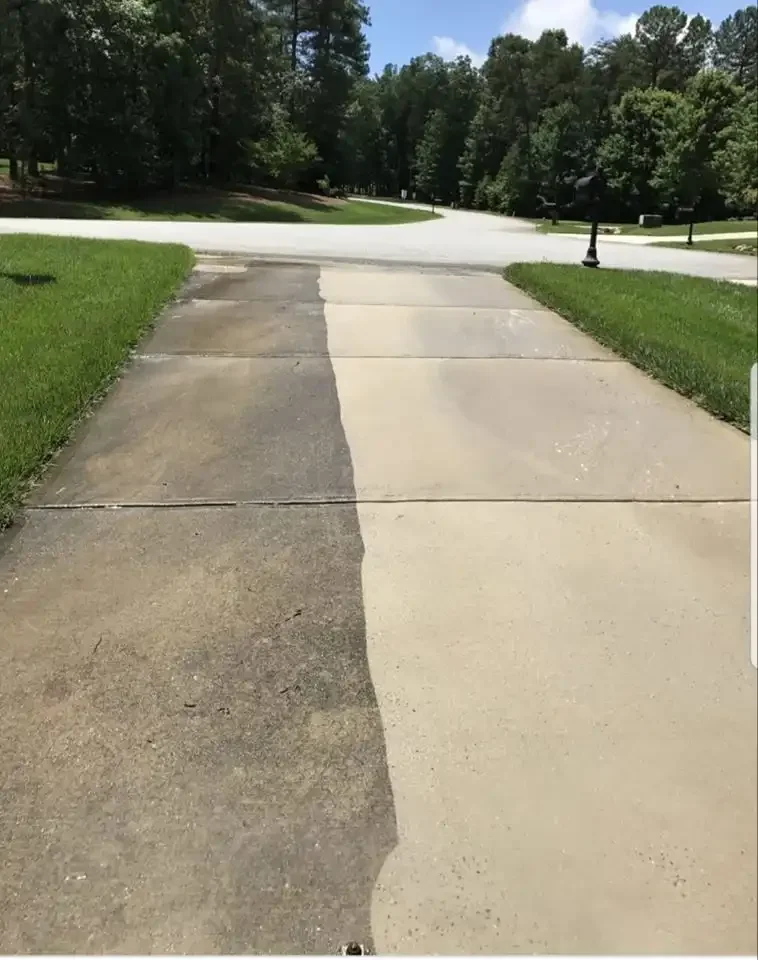 Split driveway with dirty darker concrete on the left and clean lighter concrete on the right in a residential neighborhood with grass and trees.