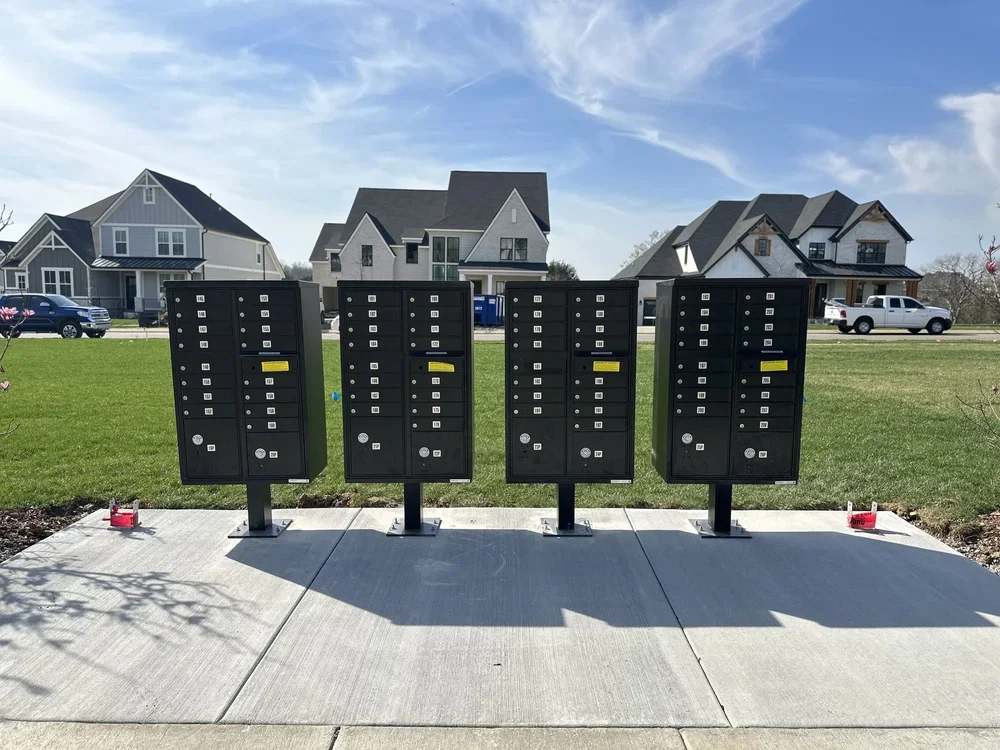 Four black parcel lockers in a residential neighborhood on a concrete sidewalk.