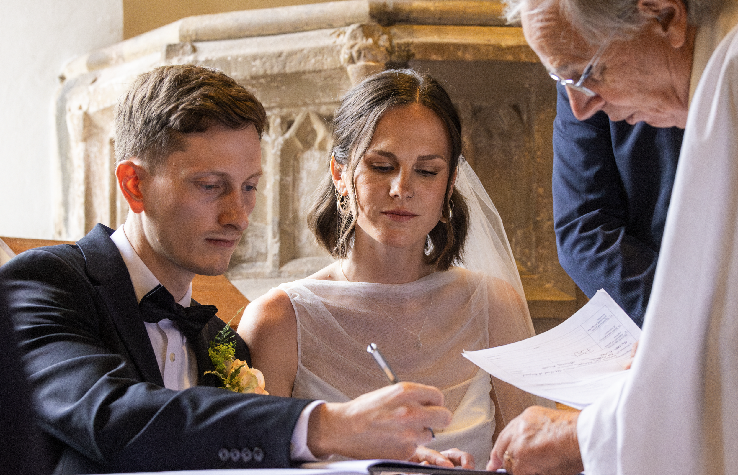 Bride and groom signing wedding documents with officiant in a church.