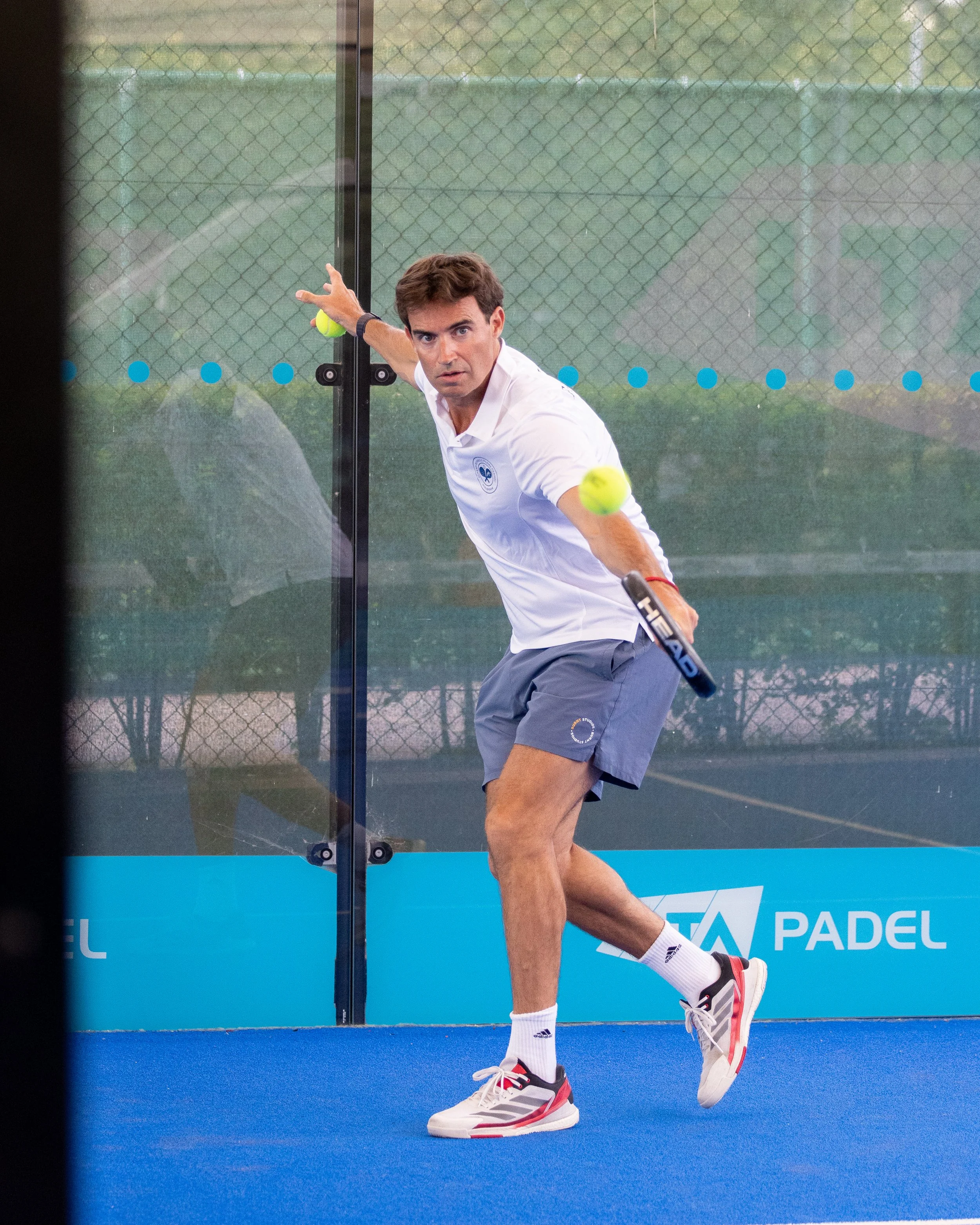 A man playing padel tennis on an outdoor court, hitting a ball with a racket, with a fence in the background.