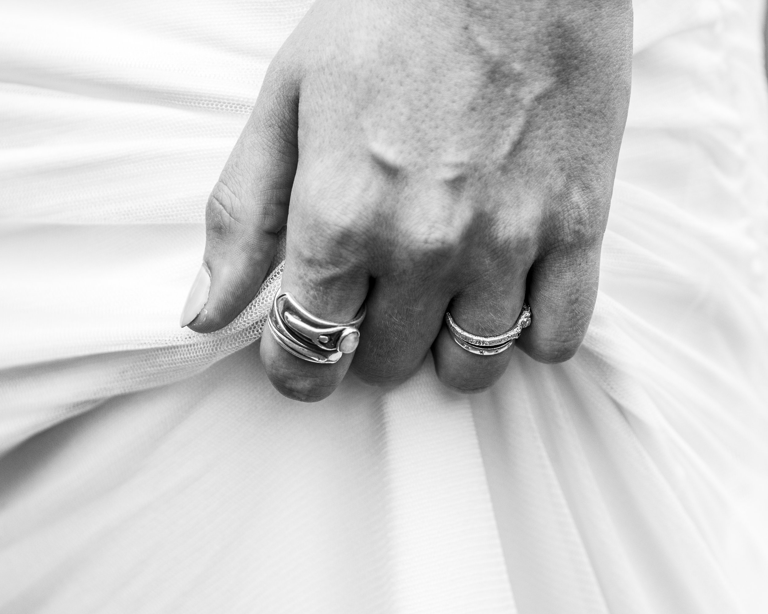 Close-up of a person's hand with rings, grasping fabric of her wedding dress.