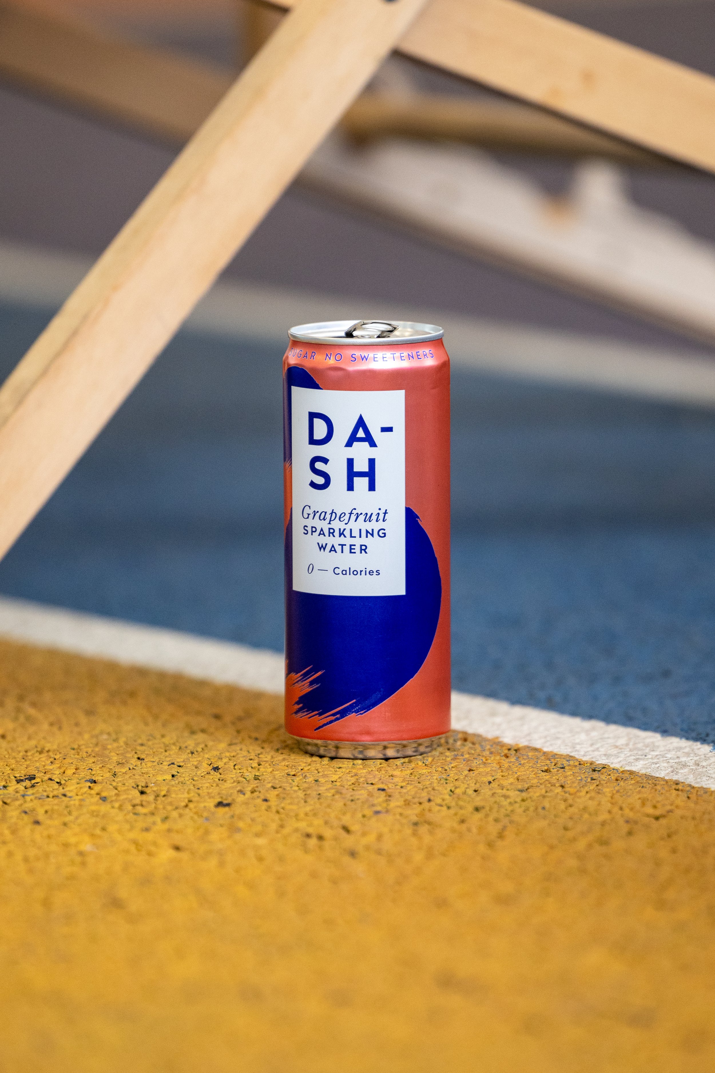 A can of Dash grapefruit sparkling water on a yellow textured stair step with a blue and gray background.