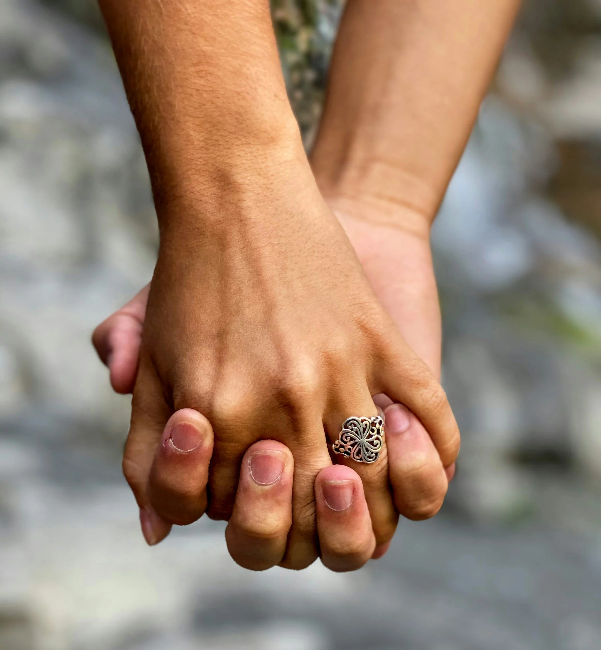 Two people holding hands, one person wearing a silver ring with intricate designs.