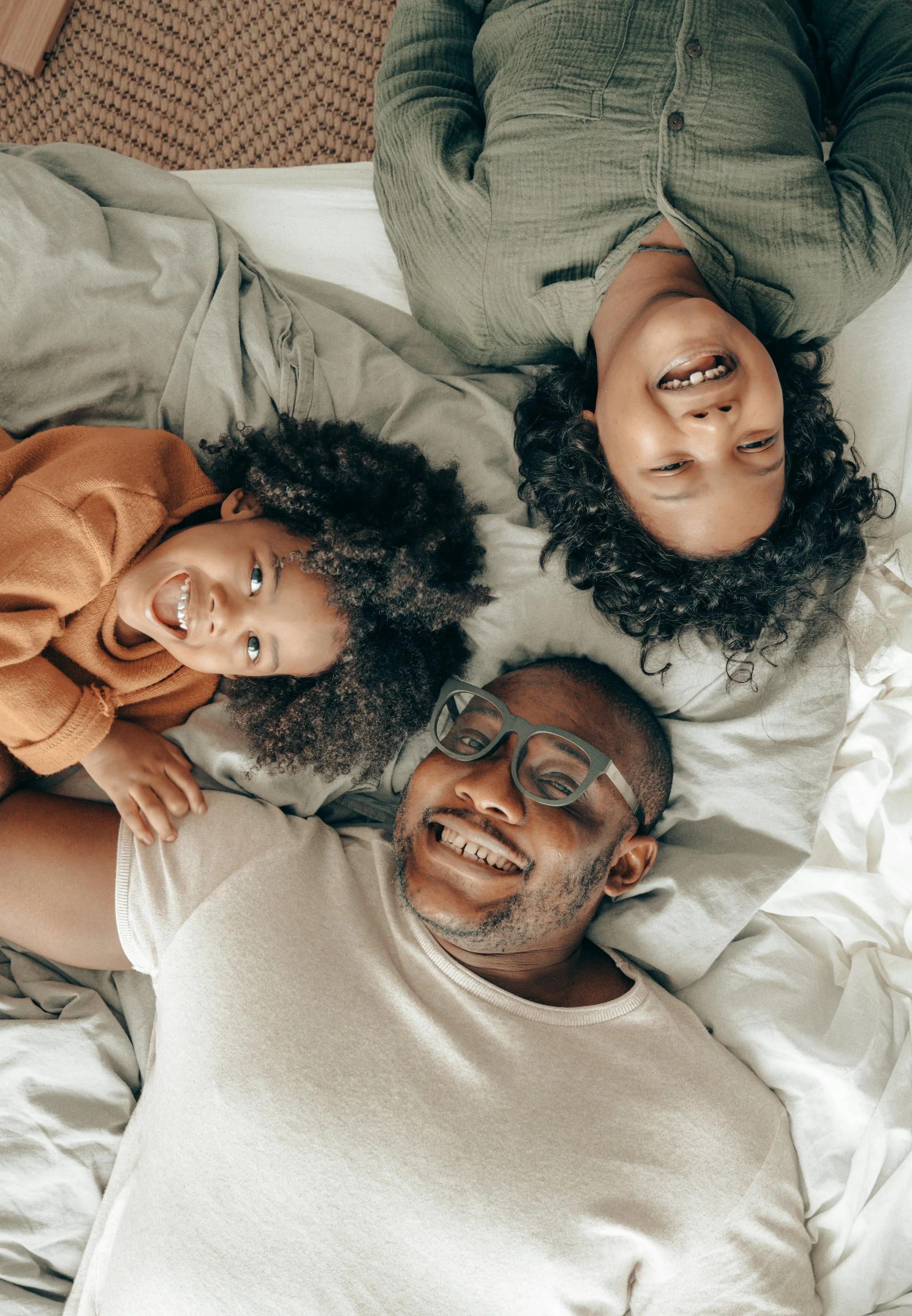 A family of three lying on a bed and smiling, viewed from above.