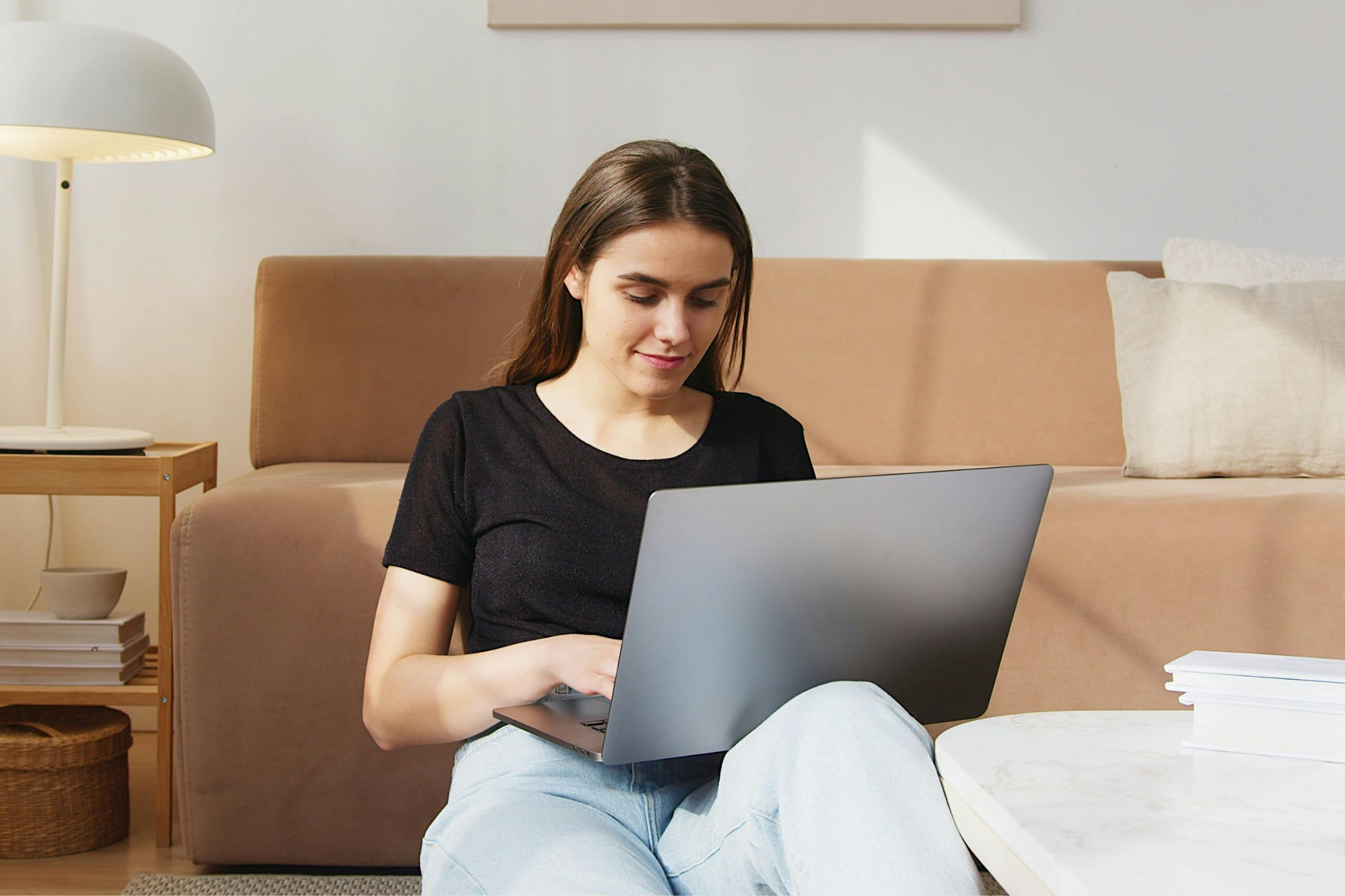 A young woman with brown hair sitting on a sofa, using a laptop in a cozy living room.