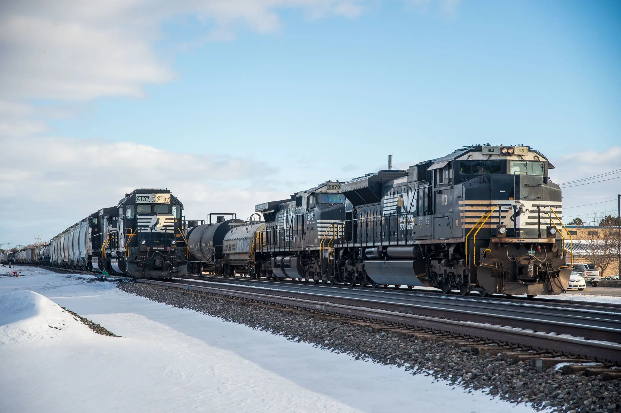 A freight train with black locomotives traveling through a snowy landscape on a clear day.