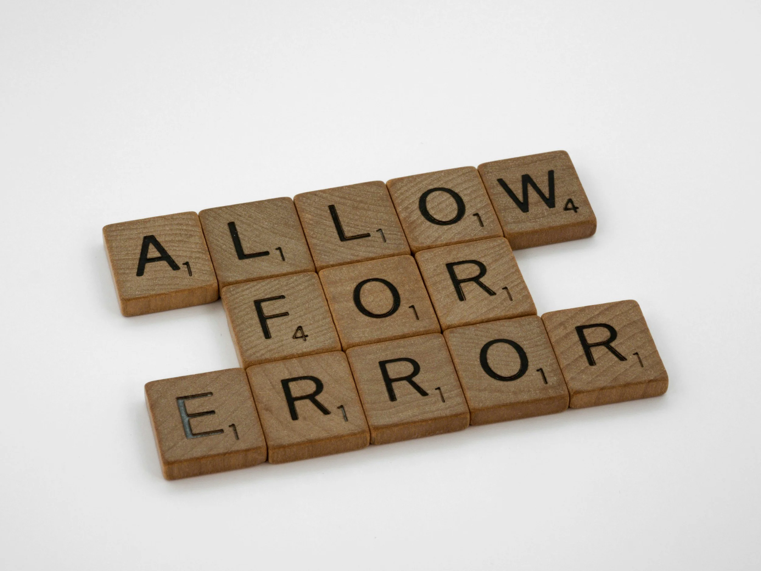 Wooden Scrabble tiles spelling the word "ALLOW" on a white background.